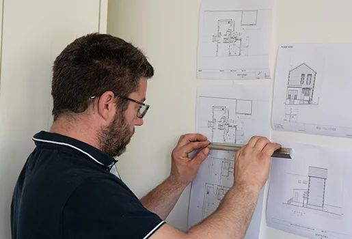 Homme barbu mesurant des plans architecturaux sur un mur blanc avec une règle à Cormeilles-en-Parisis dans le Val d'Oise 95