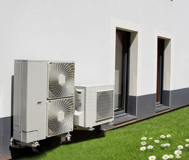 Unités de climatisation et pompe à chaleur sur un mur blanc, avec pelouse et marguerites à Cormeilles-en-Parisis dans le Val-d’Oise 95