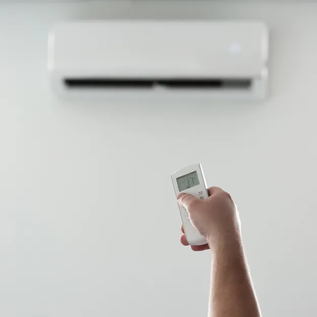 Main tenant une télécommande de climatiseur, l'unité murale est floue en arrière-plan à Cormeilles-en-Parisis dans le Val-d’Oise 95